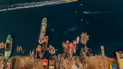Aerial view of boats on deep blue water, with some docked at a shoreline and others in motion leaving white wakes.